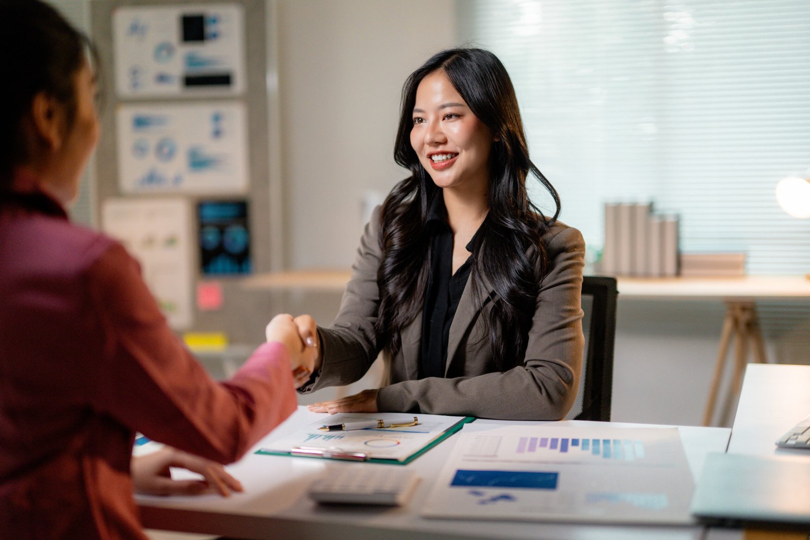 Professional women concluding successful negotiation, exchanging handshake in corporate workspace