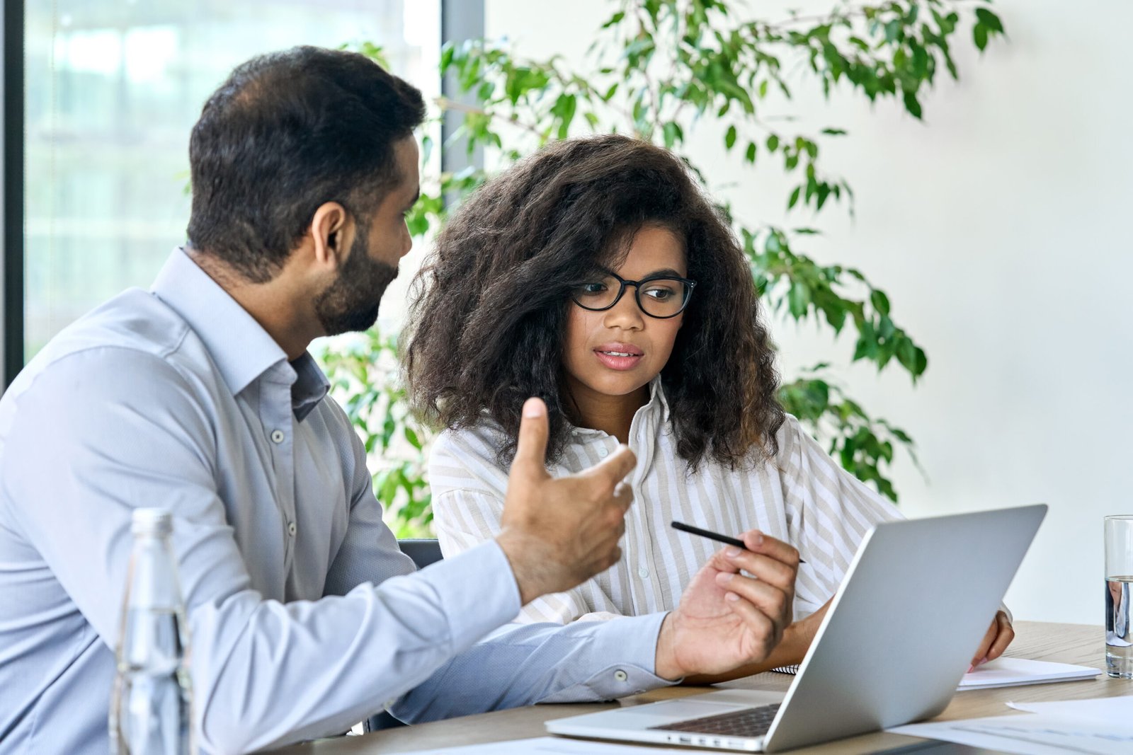 Executive manager banker indian businessman talking to female African American customer using laptop. Diverse multiethnic professional partners group discussing financial plan at board room meeting.
