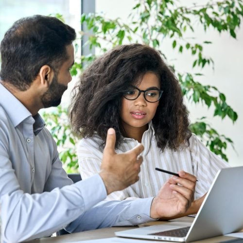 Executive manager banker indian businessman talking to female African American customer using laptop. Diverse multiethnic professional partners group discussing financial plan at board room meeting.
