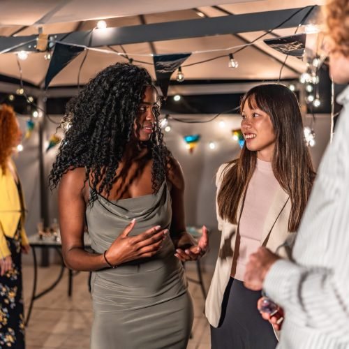 Multi-ethnic young people in elegant clothes chatting during night party at terrace