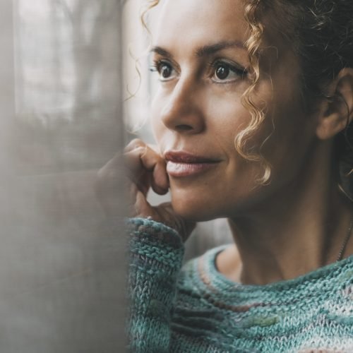 One confident lady contemplate outside the window at home with dreaming and thoughtful expression on face. Portrait of adult female people in indoor thinking leisure activity alone with window light