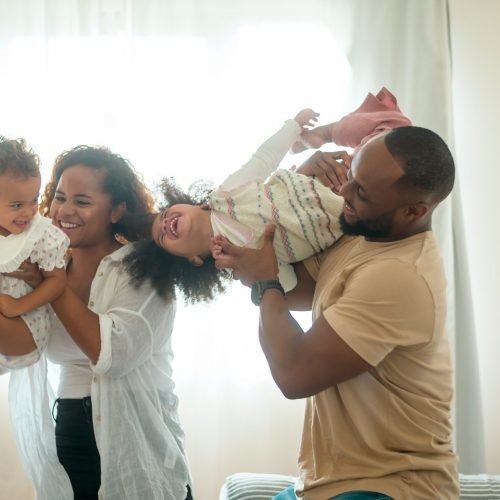 Parents with  little daughters playing on the bed in bedroom