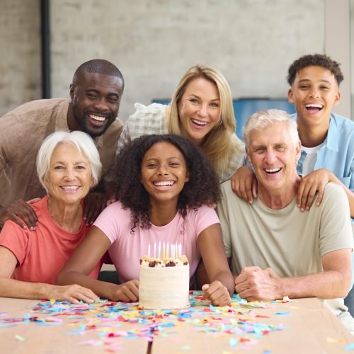Portrait Of Three Generation Family At Home Celebrating Teenage Daughter's Birthday With Cake