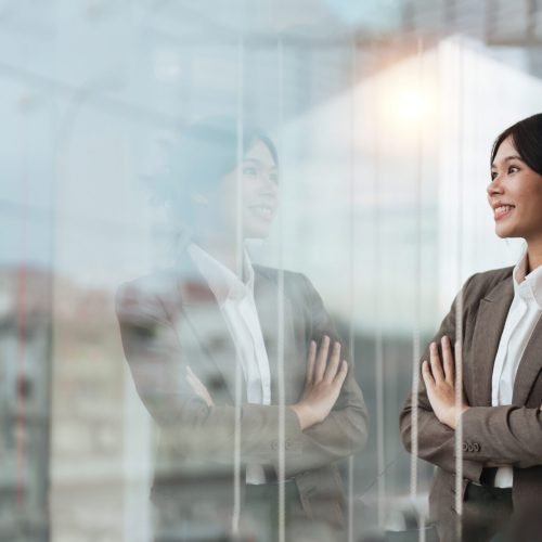 Young asian businesswoman looking out window in meeting room with confidence.